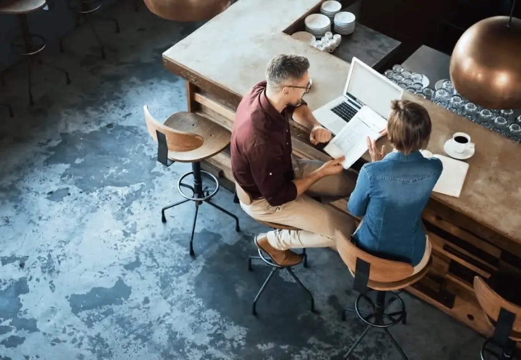 A man and woman sat at a table with a laptop browse a printed financial report